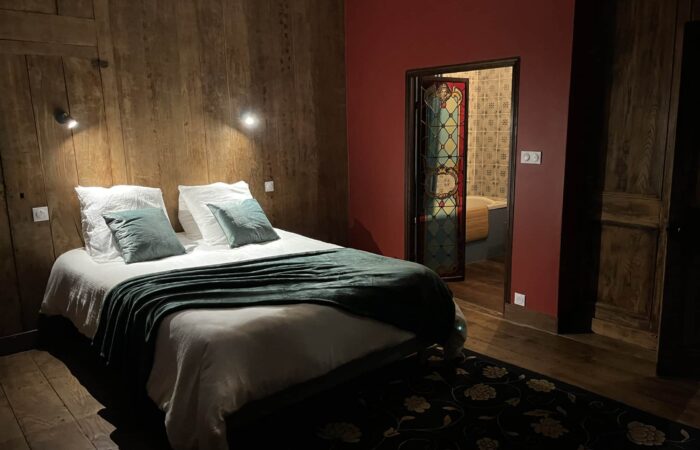 Chambre avec un lit confortable, des murs en bois sombre et une porte vitr&eacute;e d&eacute;cor&eacute;e de vitraux